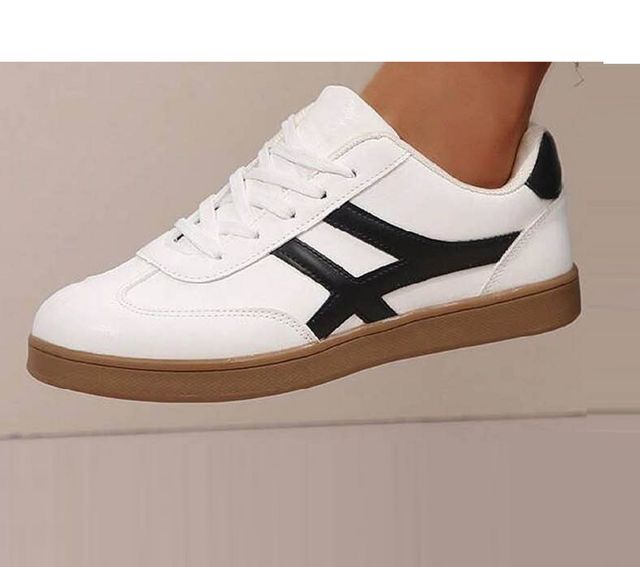 White sneaker with black stripe and brown sole on a neutral background