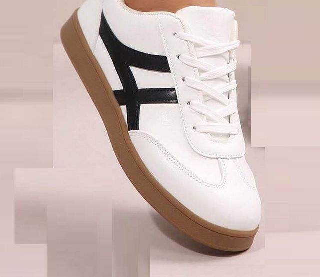 White sneaker with black stripe and brown sole on a light pink background