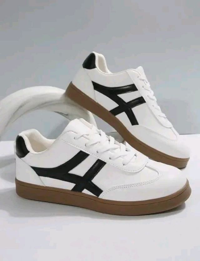White sneakers with black accents and brown soles on a light gray background