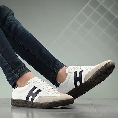 White sneakers with black accents worn by a person on a gray tiled floor.