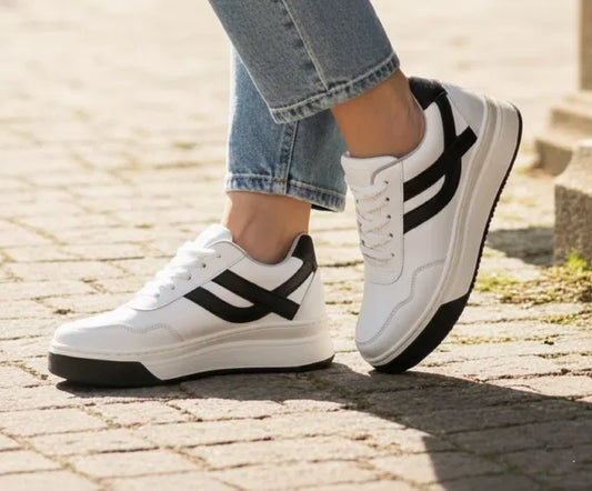 White sneakers with black stripes worn on a paved surface