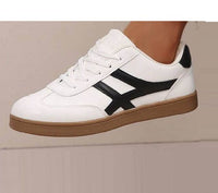 White sneaker with black stripe and brown sole on a neutral background